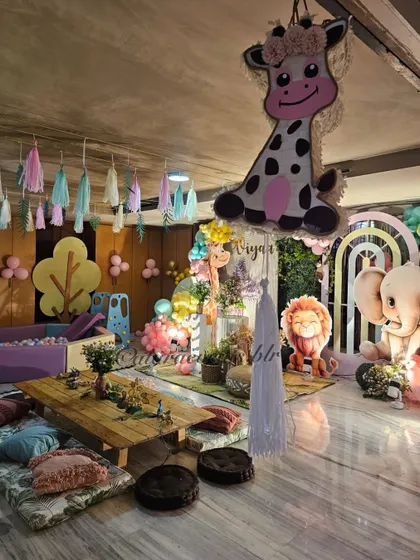 This pastel jungle setup is perfect for a "Wild One" first birthday, with low seating, a ball pit, and adorable animal cutouts like a giraffe, lion, and elephant.