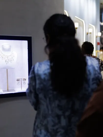 A guest admires a beautifully lit display case showcasing a statement necklace set at our Hyderabad store during an exclusive evening event.