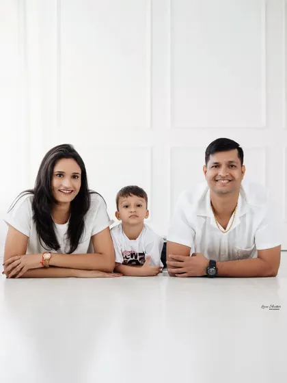 A relaxed family portrait, lying down together in the studio. The simple white outfits and clean background keep the focus on their happy faces.