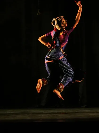An energetic leap captured against a dark stage, emphasizing the dancer's form and the feeling of flight. This is from the 'Shringara Sharanagati' production.
