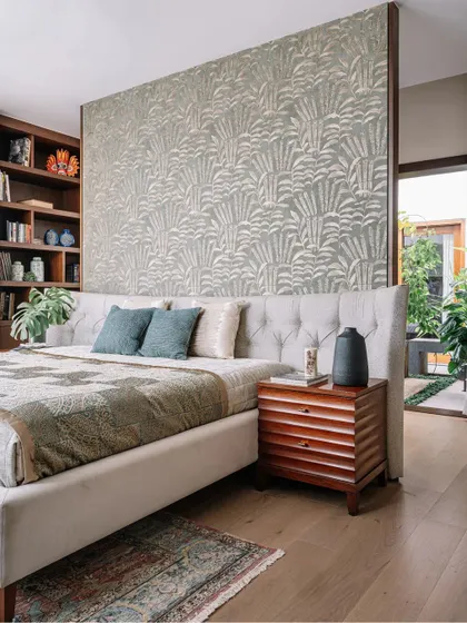 This bedroom combines comfort with clever design. A beautiful floral wallpaper creates a feature wall that doubles as a partition, with a built-in bookshelf behind the bed for storage. The tufted wingback bed adds a touch of classic elegance.