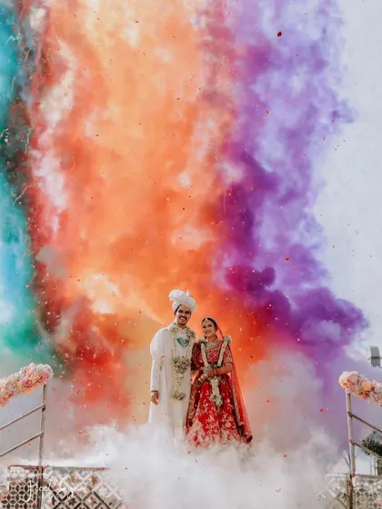 The couple stands proudly as a rainbow of colored smoke erupts behind them, creating a powerful and artistic wedding portrait.