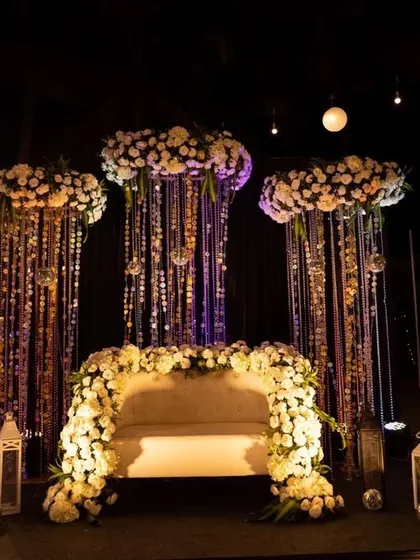 A glamorous Sangeet seating area with a backdrop of hanging crystals and disco balls. The stage is framed with white flowers, creating a chic and dramatic look perfect for a night of performances.