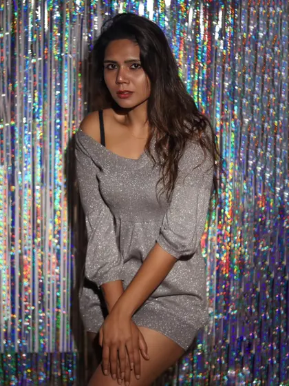 A moody and direct portrait against a shimmering studio backdrop. The contrast between the subject's expression and the festive background is compelling.
