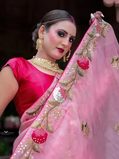 A close-up shot where the model holds up the embroidered pallu of her saree, framing her face and showcasing the detailed threadwork.