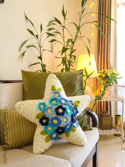Let your decor shine with this Star Blossom Cushion. The star shape offers a touch of whimsy, while the cluster of blue crochet flowers adds delicate, handcrafted beauty.