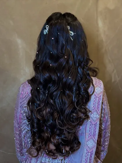 A romantic hairstyle for a sangeet, with soft curls and delicate pearl and bow accessories.