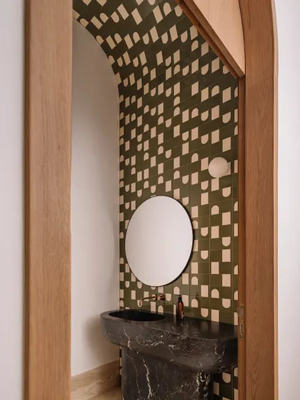 This powder room features a bold, graphic tile pattern in olive green and cream that dances up the arched wall, paired with a monolithic jet-black stone sink.
