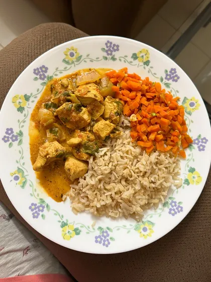 This plate features brown rice with chicken curry and a side of sautéed carrots.