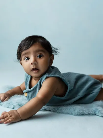 A simple and sweet portrait of a baby enjoying tummy time on a soft blue rug. The minimalist setup keeps the focus entirely on the baby.