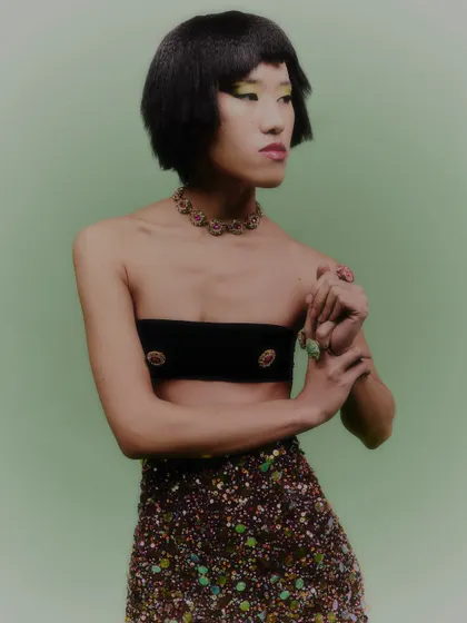 A portrait that highlights the jeweled choker and the model's playful expression. The styling is confident and fashion-forward.