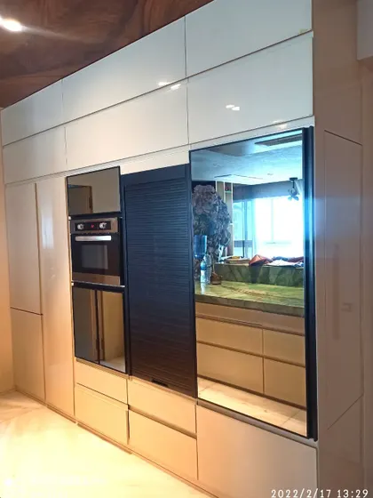 The tall unit in the Jhamdar kitchen features a mix of finishes, including a black rolling shutter and mirrored panels that add depth and reflect light, making the space feel larger.