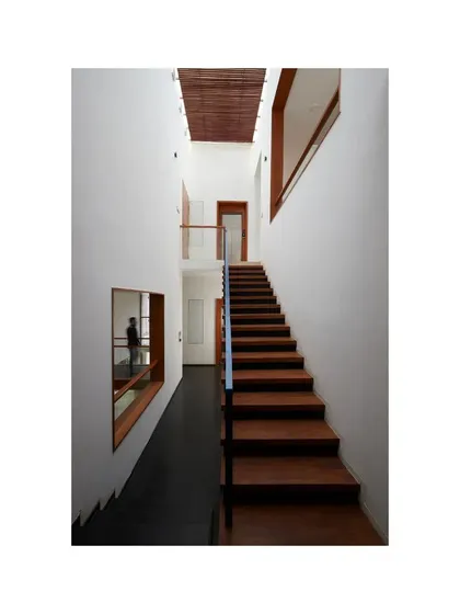 A floating wooden staircase in a double-height space within the Vikas Residence. The simple, clean lines of the stair and the warm tone of the wood stand in contrast to the cool, dark flooring, creating a moment of visual and material interest.