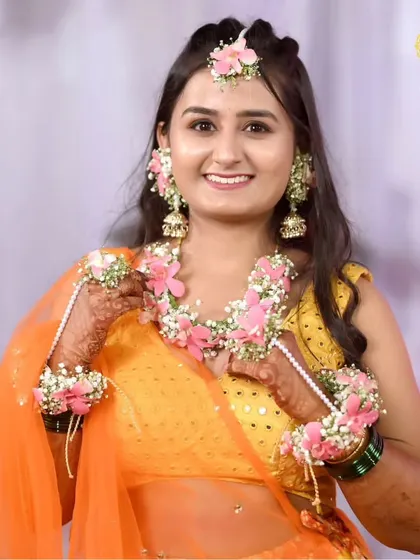 A radiant Haldi bride glowing in our custom-designed floral jewellery. This set, featuring delicate pink flowers and baby's breath, is handcrafted to perfectly complement the vibrant orange of her outfit, making her Haldi ceremony truly unforgettable.