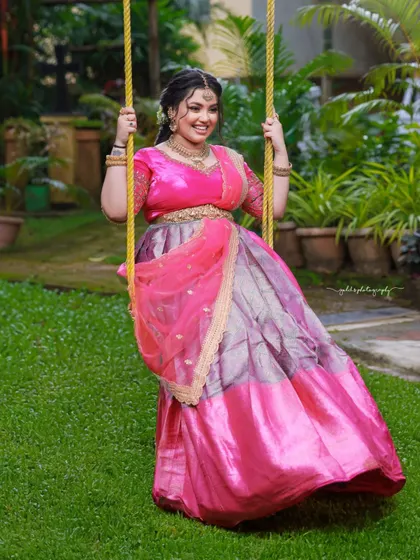 A cheerful and vibrant outdoor shoot featuring a model in a pink and purple half-saree. The playful poses on a swing and the bright colors capture a youthful and joyous spirit.