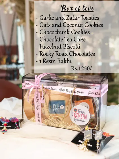 The "Box of Love" hamper is a transparent gift box packed with a delicious assortment. It includes garlic and zatar toasties, oats and coconut cookies, chocochunk cookies, a chocolate tea cake, and hazelnut biscotti.