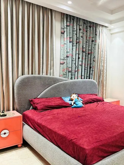 A simple and sweet kid's bedroom with a comfortable bed, playful printed curtains, and a pop of color from the orange bedside table.