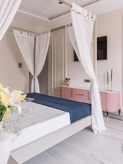 A full view of the 'Modern Muse' bedroom, showcasing the four-poster bed, the pink console, and the overall light and airy feel created by the white marble floors and sheer curtains.