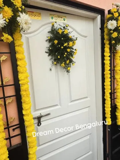 Simple yet beautiful Haldi decor for the entrance of a home. The marigold garlands and floral bunches on the door create a warm and traditional welcome.