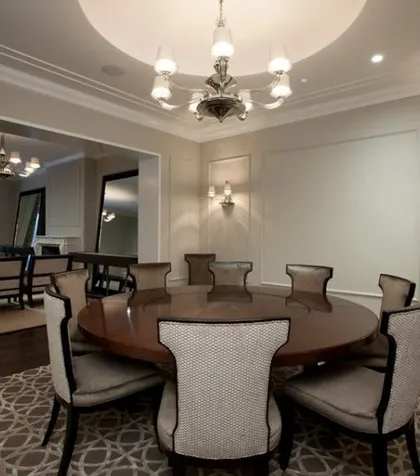 A formal dining room with a grand round table, perfect for conversations, set under a classic chandelier with elegant wall sconces.