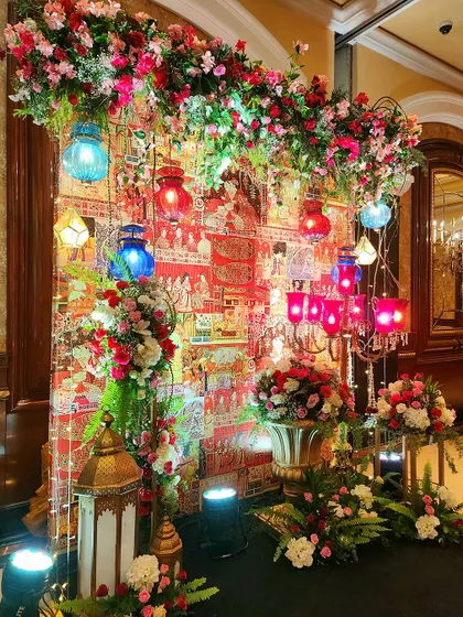A vibrant and colorful photo corner for the Sufi Night. The backdrop features traditional Indian textile art, decorated with hanging lanterns and lush floral arrangements.