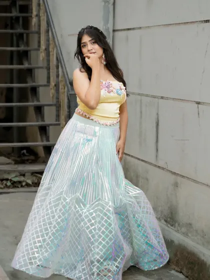 A full-length portrait in a whimsical, pastel-colored lehenga. The industrial-style staircase in the background provides an interesting contrast.