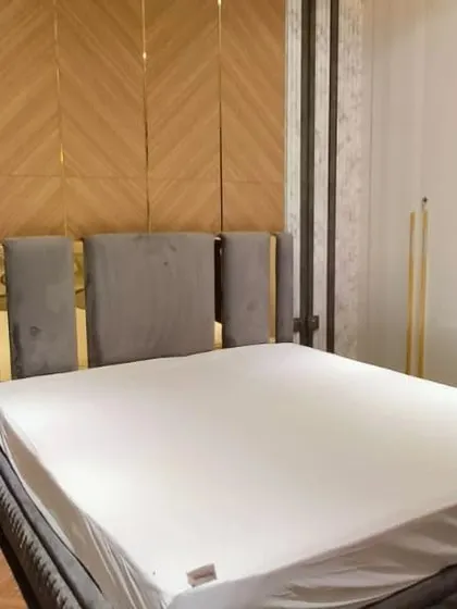 A close-up of the custom bed with a grey upholstered headboard, set against a geometric wood-paneled wall. The design uses a mix of textures to create a rich, luxurious feel.
