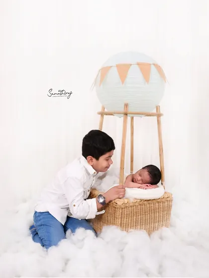 Including siblings in themed shots can be so much fun. Here, a proud big brother looks on as his new baby sister rests in the hot air balloon basket, creating a sweet story of shared adventure.