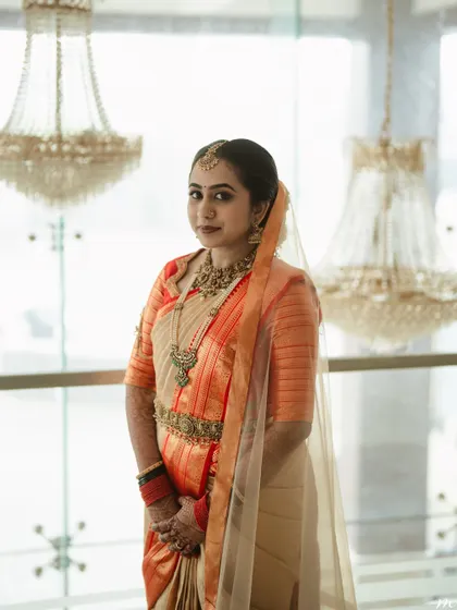 An indoor portrait showing the bride's elegant look against a backdrop of chandeliers. The makeup is polished, with a focus on a smooth base and defined features.