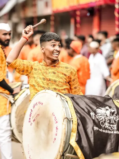 A dhol player with a wide smile, his stick raised, captured in a moment of pure joy and energy.