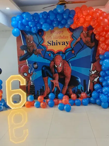 A dynamic Spiderman-themed 6th birthday party setup. This decoration includes a custom character backdrop, a bold red and blue balloon arch, a large light-up number '6', and a Spiderman cutout figure, bringing the superhero action to life.