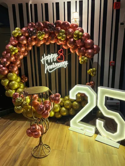 A 25th anniversary celebration with a balloon ring in chrome colors. The large marquee numbers and a 'Happy Anniversary' neon sign make for a stylish photo corner.