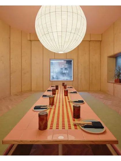 A private dining room at Lucky Chan, featuring a long table with a custom tile runner. The space is enclosed with wood paneling and illuminated by a large, handmade raw silk lamp, creating a warm and intimate setting.