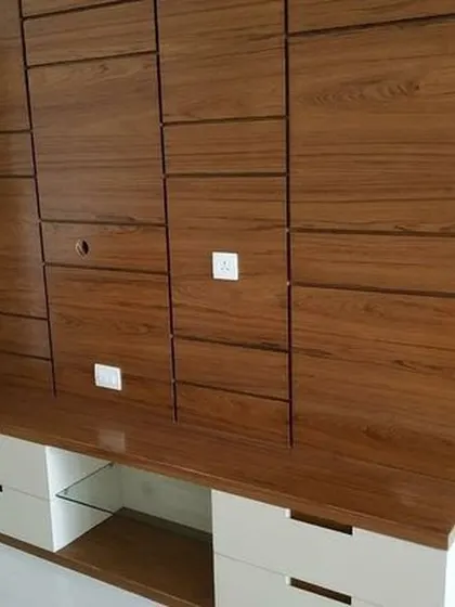 A close-up of a custom-designed TV unit with a unique textured wood paneling. The design cleverly conceals wiring and offers a mix of open and closed storage with sleek white drawers at the base.