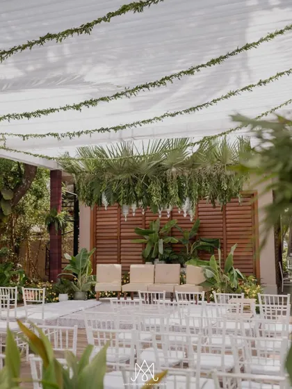 The full view of the mandap, with a white fabric canopy and a lush hanging centerpiece of palm fronds, creating a serene and natural ambiance.