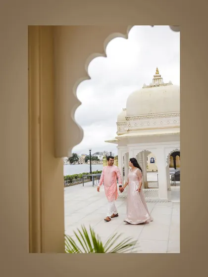A post-wedding shot of a couple walking by the lake in Udaipur, framed by a palace arch.