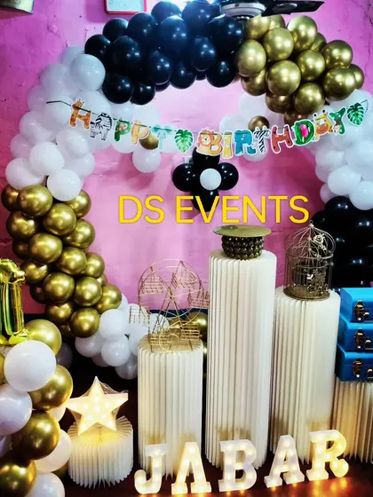 This elegant black, white, and gold theme is a stylish option for a first birthday party. The decor features a circular balloon arch, light-up marquee letters for the name, and modern ribbed plinths for the cake display.