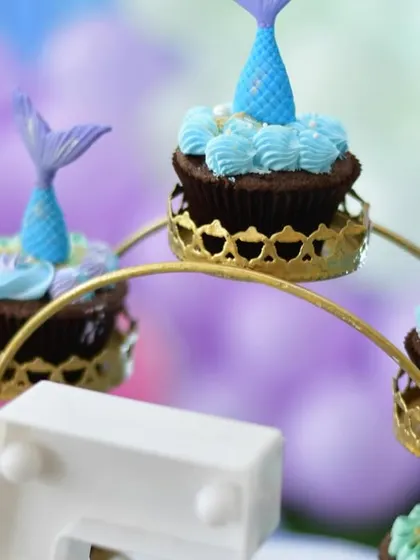Themed cupcakes that perfectly match the mermaid party decor. Each cupcake is topped with a detailed, edible mermaid tail, displayed on a decorative ferris wheel stand.