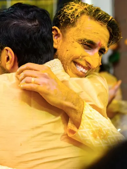 A happy, yellow stained hug between the groom and a friend. The camaraderie and fun of the Haldi ceremony are on full display.