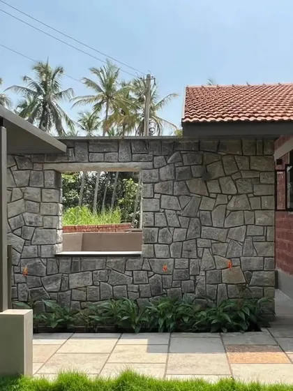 A wall of random rubble masonry provides a rugged, textural contrast to the smooth, finished surfaces of this Mangalore holiday home. The window opening is left without a frame to emphasize the thickness of the stone wall.