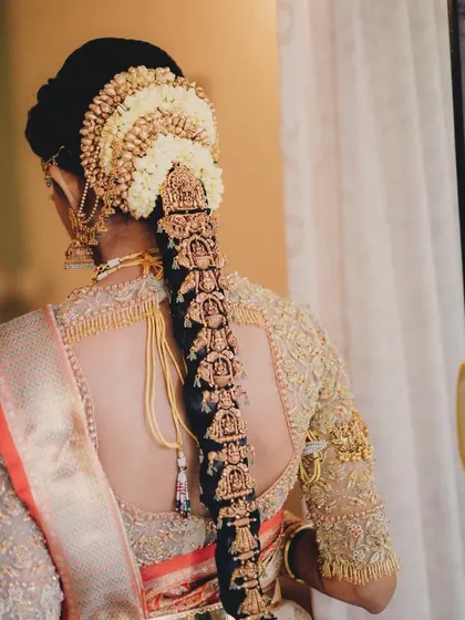 A back view of a classic South Indian bridal hairstyle. The neat bun is adorned with jasmine flowers, leading into a long braid decorated with traditional gold ornaments.