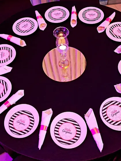 A chic table setting for a 'Hello Gorgeous' themed party. The black and white striped plates with pink accents and neatly folded napkins create a stylish and sophisticated look.