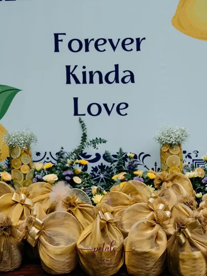 The favor table at the citrus-themed Haldi, with a "Forever Kinda Love" sign. The gifts are wrapped in gold fabric, complementing the yellow and blue color scheme.