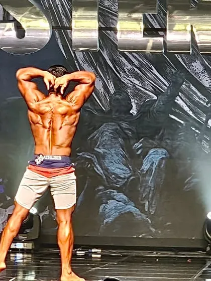 A back double-bicep pose on stage. This showcases the definition and symmetry required to compete at a high level, achieved through natural bodybuilding.