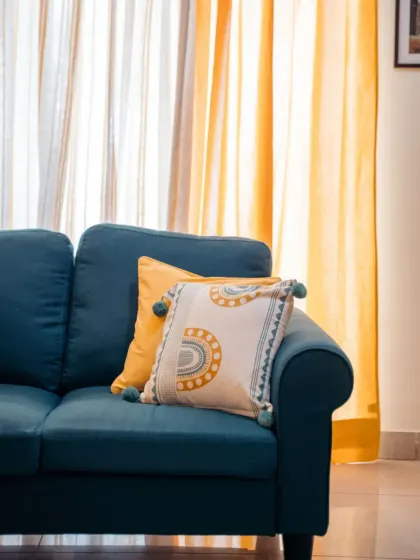 A close-up of the details. Our 'Aura' cushion cover with its playful tassels sits beautifully against the teal couch, picking up the mustard tones from the layered curtains in the background.