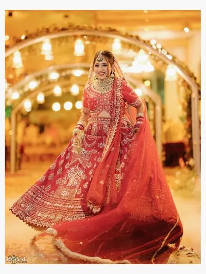 A radiant portrait of the bride twirling in her red wedding lehenga, captured under a beautifully lit archway.