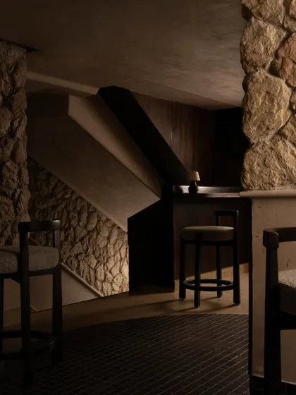 A corner of Call Me Ten, a Japanese-inspired restaurant in Delhi. The space is a study in minimalism and materiality, where rough stone walls and dark wood create a serene, almost monastic, atmosphere.