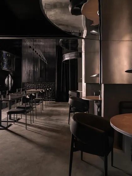 The main dining area of Lair, where curved metal partitions create semi-private booths. The reflective surfaces create a disorienting yet captivating play of light and shadow.