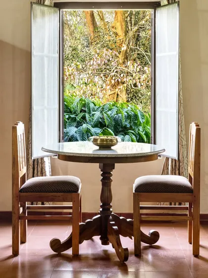A small dining table for two, perfectly positioned in front of a window that opens to a lush green view. This intimate setting captures a romantic and peaceful moment at the resort.