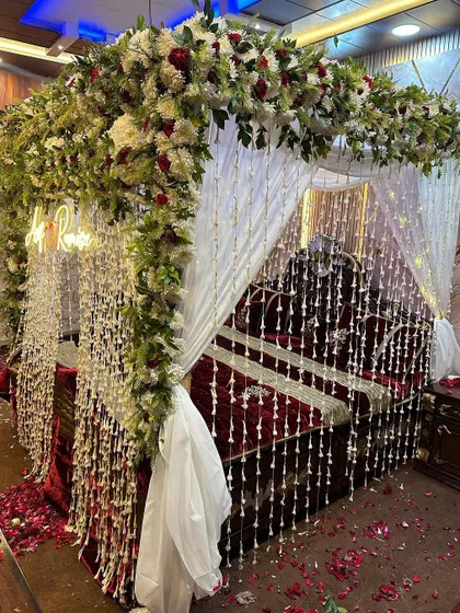 A beautiful wedding night setup with a bed decorated with a floral arch and hanging strings of flowers. The decor is rich and traditional.